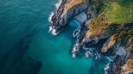 Aerial drone shot of a coastal headland, capturing the dramatic meeting of land and sea with rugged cliffs and waves crashing below.
