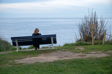 Woman sitting on a bench overlooking the ocean in solitude