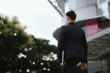 A determined young businessman in a city, confidently working on his laptop outdoors, dressed in a...