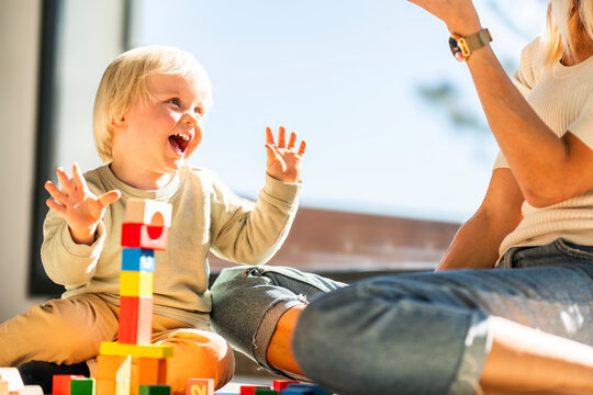 Happy boy having fun playing building bricks with mother at home