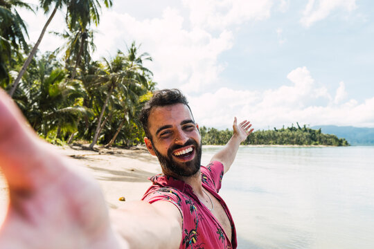 Cheerful man taking selfie with arms outstretched at beach