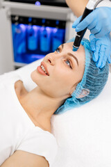 A cosmetologist wearing gloves performs vacuum cleaning and polishing of the facial skin of a middle-aged woman in a cosmetology clinic. Professional moisturizing and rejuvenating hardware procedures.