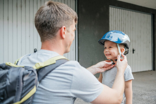 Father fastening safety helmet of son at back yard