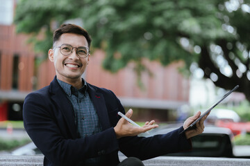 A cheerful young Asian businesswoman in a modern city, smiling confidently while using her smartphone outdoors, dressed in a professional suit, embodying success and digital connectivity.