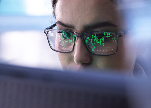Focused businesswoman with reflection of stock market data on eyeglasses