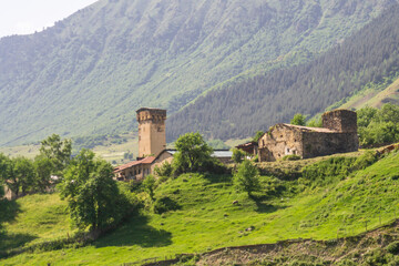 Fototapeta premium An old defensive tower next to a residential building. A clearing with green grass and mountains covered with trees