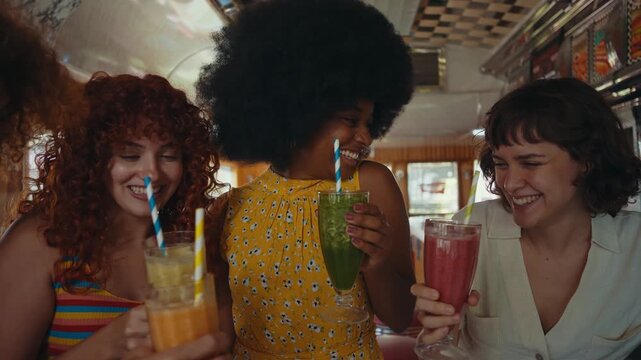 Cinematic footage about a group of multi-ethnic friends eating and having fun in an american styled diner restaurant. Drinking colored fruit milkshakes.