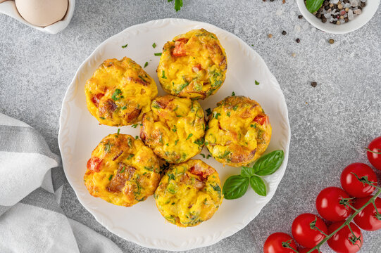 Egg muffins or egg bites with bacon, cheese, vegetables and herbs on a white plate on a concrete background. Healthy breakfast.