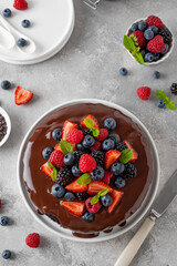 Delicious chocolate cake with chocolate glaze and fresh berries on a white plate on a gray concrete background.