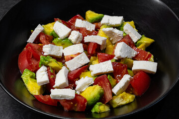 Fresh red tomato, avocado and bryndza or feta salad with olive oil in black dish close-up view from top, healthy eating.