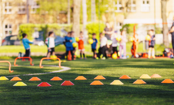Sports Training Equipment on Outdoor Sports Field. Training Cones and Markers on Artificial Grass Pitch. Group of School Children With Balls in Blurred Background