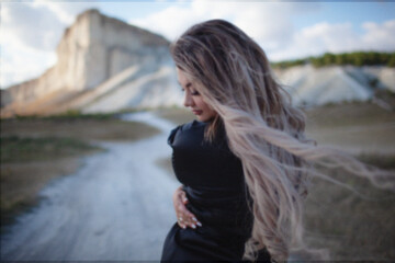 A woman plus size dressed in a dress walking against the background of a white mountain. Beautiful girl with a long hair developing in the wind travels