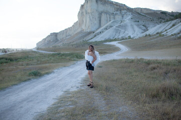 A woman plus size dressed in a dress walking against the background of a white mountain. Beautiful girl with a long hair developing in the wind travels