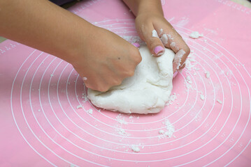 Female hands preparing sugar paste on a pink cake mat.