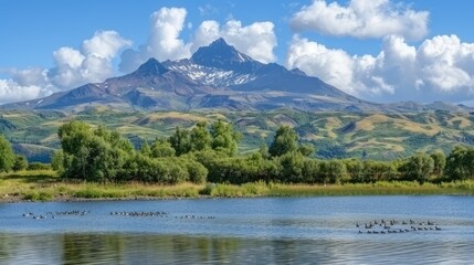 Obraz premium A tranquil riverbank with smooth stones meets the calm waters, bordered by verdant mountains and a cloudy sky, showcasing the beauty of nature in a remote location