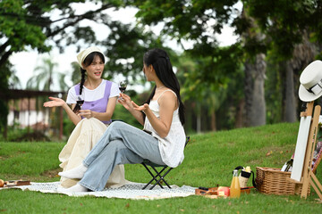 Young female friends drinking wine and enjoys a picnic on a blanket in a park
