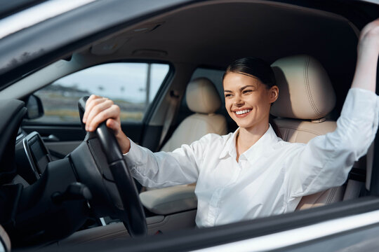 Woman driving new car in a parking lot, smiling with hand on steering wheel