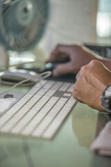 close up of man's hands holding computer mouse and typing on keyword on a table day time at office  