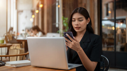 An attractive Asian businesswoman is using her smartphone while working remotely from a cafe.