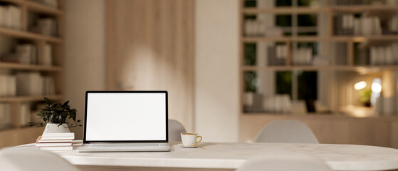 A laptop computer with a white-screen mockup on a white marble table in a contemporary cozy room.