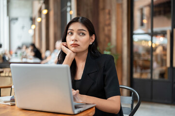 A thoughtful Asian businesswoman is concerned about her job while working remotely from a cafe.