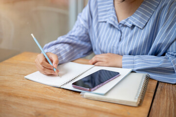 A cropped image of a woman writing something in a book or doing homework at a table in a cafe.