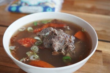 A bowl of ribs soup with meat, tomatoes, carrots, and scallions