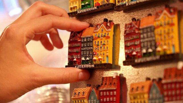 Rows of colorful souvenir fridge magnets representing traditional buildings of Copenhagen. Tourist choosing magnet for memory from Denmark trip
