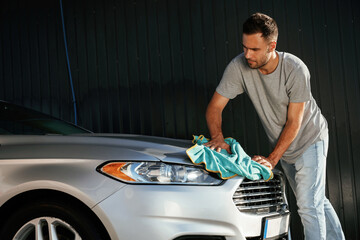 View from the side, using cloth to polish the automobile. Man is with his car outdoors