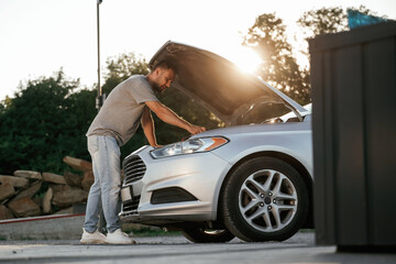 Beautiful sunlight. Hood is opened, guy is repairing the automobile. Man is with his car outdoors
