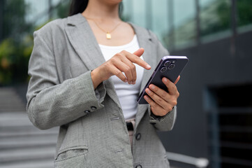 A businesswoman is reading text or replying messages on her smartphone while walking in the city.