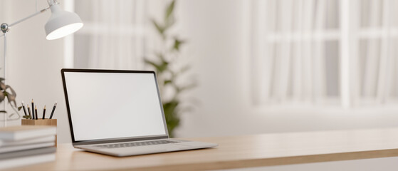 A laptop computer with a white-screen mockup and decor on a wooden tabletop in a bright room.