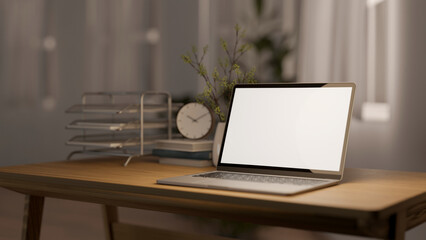A laptop computer with a white-screen mockup on a wooden table in a room at night. place of work
