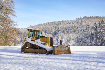 Yellow bulldozer in a field against the backdrop of a snowy forest.