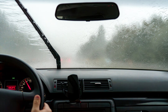 The car's windshield wipers work during rain while driving on the road.