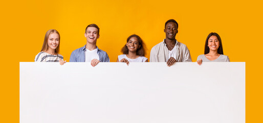 Smiling group of multiracial students standing together in row and displaying white empty placard,...