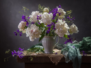 Still life with white peonies and delphinium on a dark background