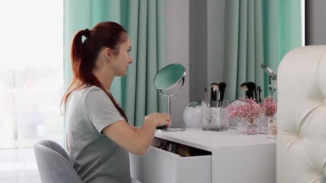 A young woman applies cream on her face while looking in the mirror in slow motion. Skincare concept. Concept of beauty routine, self-care, and daily cream use