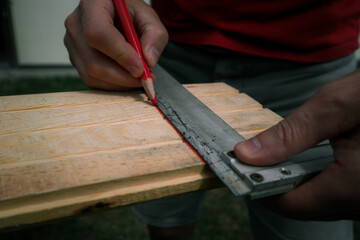 Cropped image of male carpenter marking on plank in workshop. Hands of a Caucasian carpenter man in the workshop making some marks on the wood