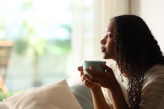 Black woman contemplating at home drinking coffee