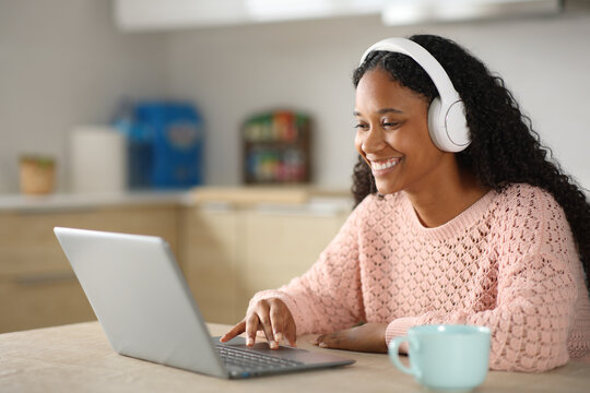 Black woman using laptop and headphone in the kitchen