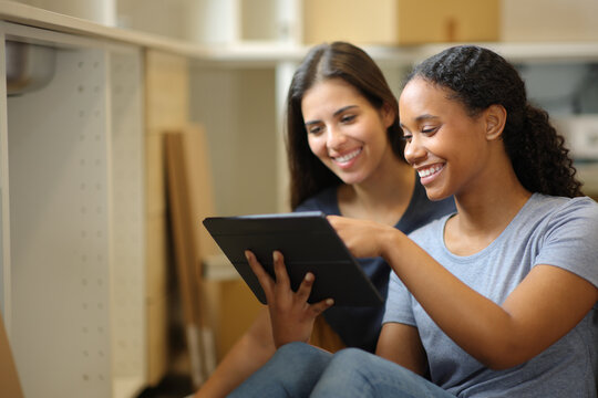 Two happy roommates checking tablet while renovating home - Powered by Adobe