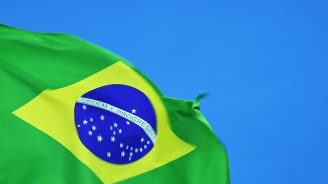 Slow motion video of Brazil flag waving on blue sky background