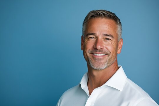 A confident middle-aged man with gray hair smiling in business casual attire against a blue background