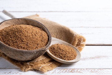 Coconut palm sugar in a coconut bowl on white wooden table background. Copy space