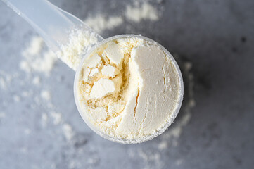 Top view of scoop with sport nutrition, protein, creatine, gainer as white powder on gray background