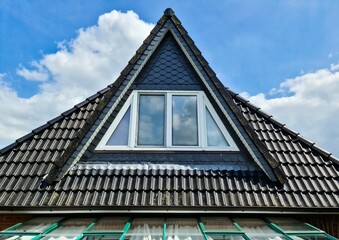 Open roof window in velux style with black roof tiles and a blue sky
