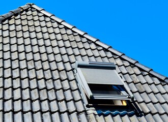 Open roof window in velux style with black roof tiles.