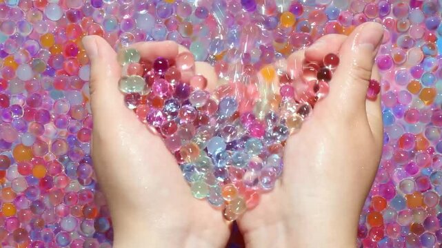 The girl's hands take a handful of multicolored hydrogel balls shining in the sun. A lot of colorful little balls smoothly move the girl's hands. View from above. Asmr. Antistress.Part 5