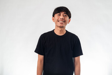 Fototapeta premium A smiling Asian man in a black t-shirt stands casually against a plain white background, perfect for professional headshots, personal branding, or casual business profile content